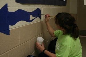 Rosa Gyuris, Academic Affairs, helps paint stenciled figures on the hallway walls at Arlington Heights Elementary School on Charter Day.